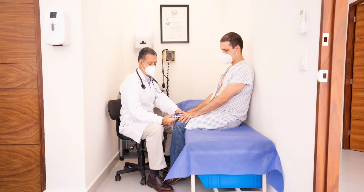 Médico de jaleco branco examinando paciente sentado na maca de um consultório