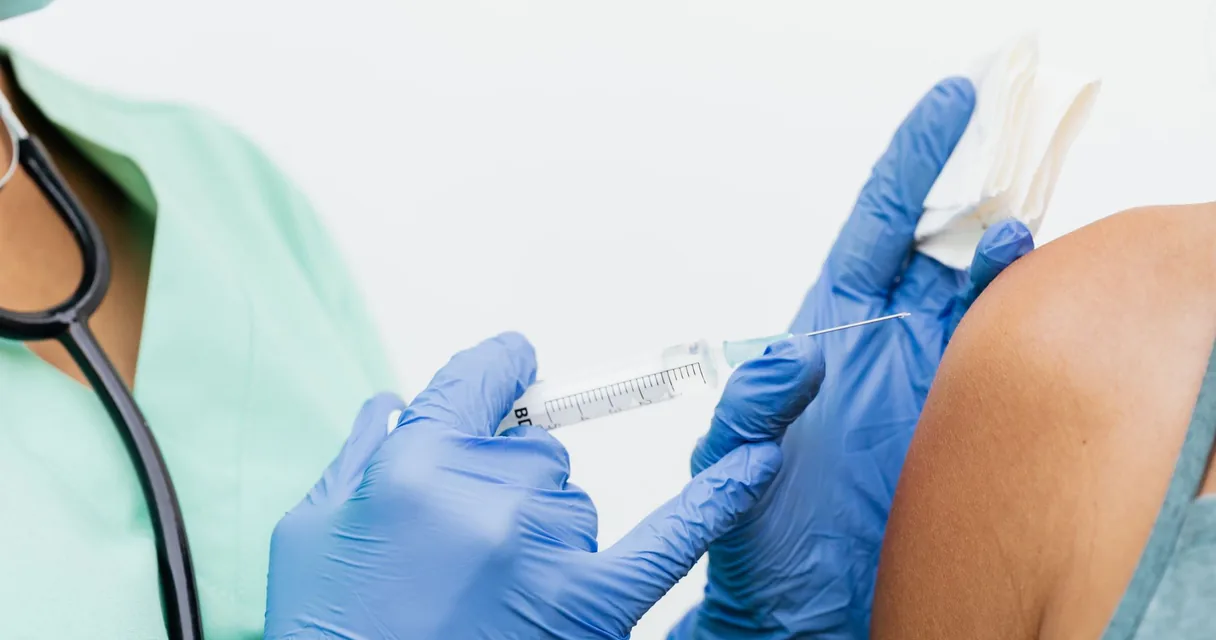 Médico aplicando injeção no ombro de paciente com luvas azuis